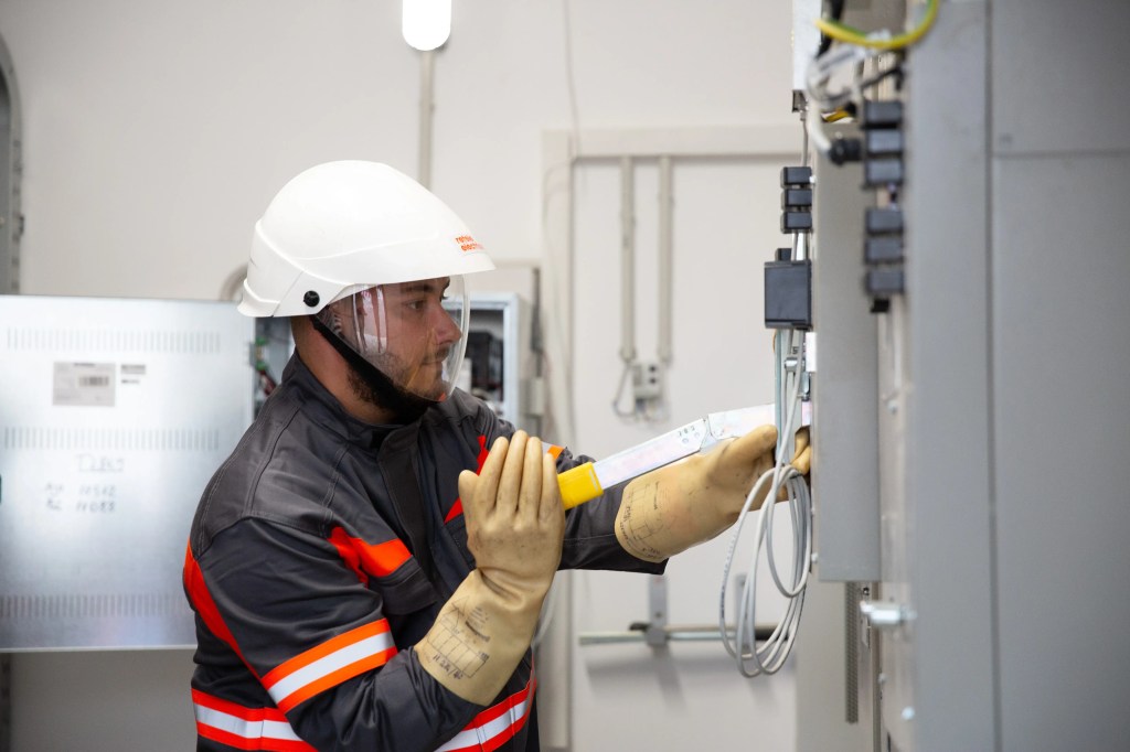 Tehnician electrician efectuand verificari la un tablou electric, utilizand echipamente de protectie