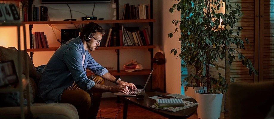 Barbat lucrand concentrat pe laptop intr-un living modern, cu iluminare ambientala calda